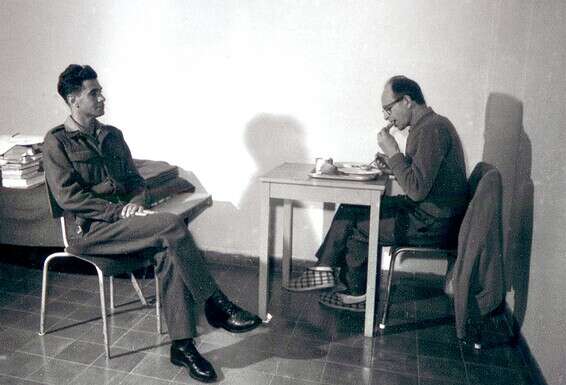 אייכמן אוכל מול שוטר, כשלרגליו נעלי בית "קיפי" ישראליות. מחשש להרעלה, אכל מהקצבת המזון של השוטרים // צילום: באדיבות משטרת ישראל