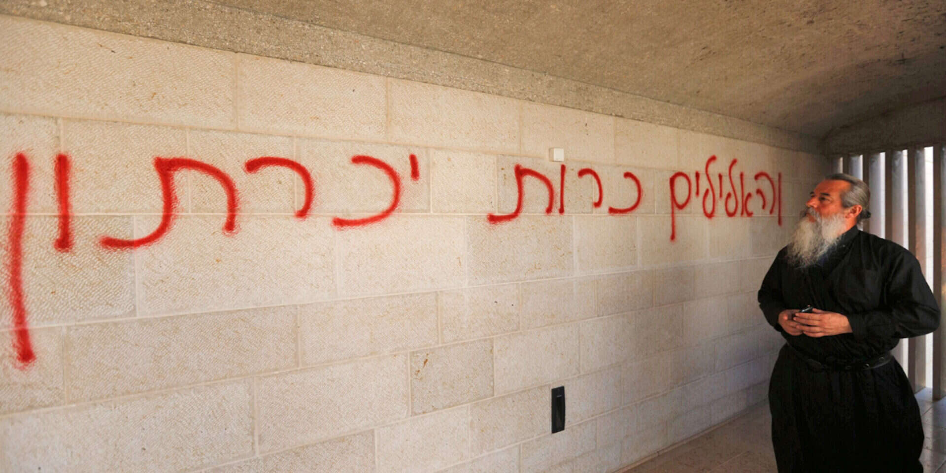 איש דת נוצרי ליד הכתובת שהשאירו המציתים // צילום: אי.פי.איי // איש דת נוצרי ליד הכתובת שהשאירו המציתים  , 