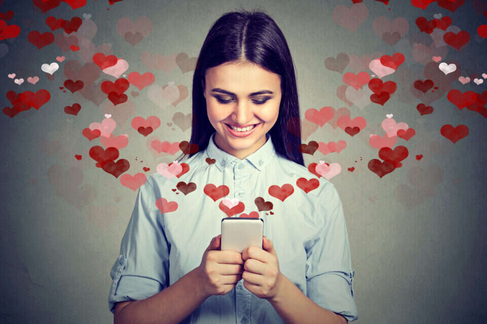 אישה מחייכת מאהבה כשהיא מחזיקה בטלפון הנייד שלה , Getty Images