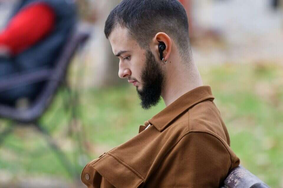 בחור צעיר עם זקן מטופח מרכיב אוזניות זעירות