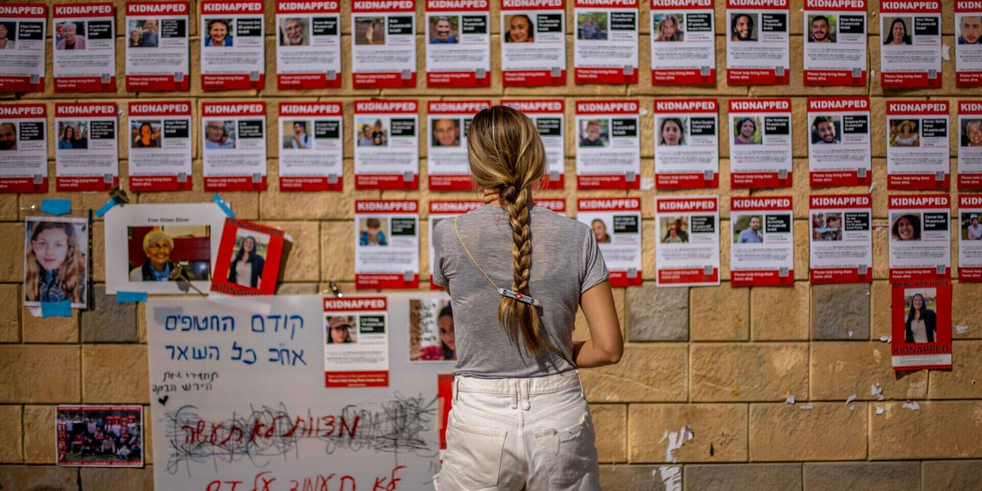 אישה מביטה בקיר עם תמונות החטופים לעזה