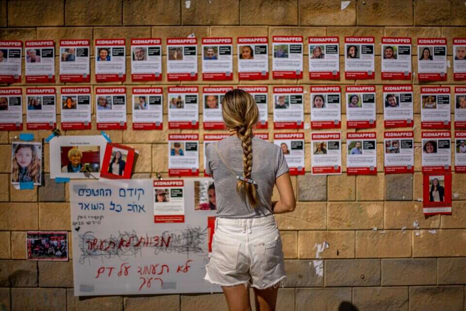 אישה מביטה בקיר עם תמונות החטופים לעזה