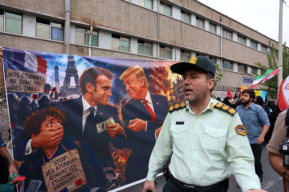 איש משמרו תהמהפכה לצד כרזה הלועגת למקרון סמוך לשגרירות צרפת , איי.א.פי